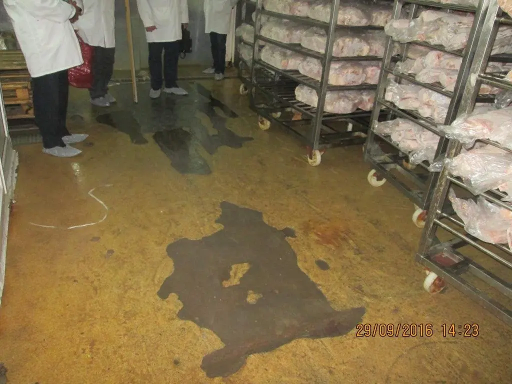 Пол производственного помещения с тёмными пятнами и отслоениями покрытия между стеллажами